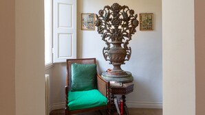 Ein Zimmer mit einem Holzstuhl mit grüner Sitzkissen, einer dekorativen Metallvase und zwei gerahmten Bildern an der Wand.