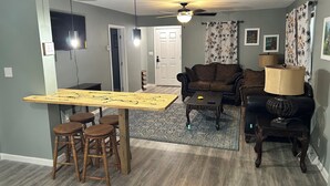 A living room with a sofa, a coffee table, a dining table with stools, and a ceiling fan. - Charming 2-bedroom cottage in welcoming Larned with AC,WiFi, full over full bunk (Larned)