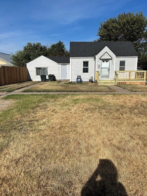 A residential property with a fenced yard, a detached garage, and a house with a front porch. - Charming 2-bedroom cottage in welcoming Larned with AC,WiFi, full over full bunk (Larned)
