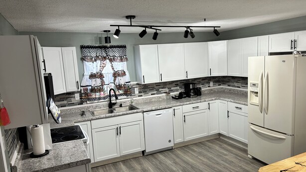 A modern kitchen with white cabinets, a granite countertop, a built-in dishwasher, and a refrigerator. - Charming 2-bedroom cottage in welcoming Larned with AC,WiFi, full over full bunk (Larned)