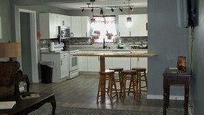 A modern kitchen with white cabinets, a central island with stools, a microwave, and a stove. - Charming 2-bedroom cottage in welcoming Larned with AC,WiFi, full over full bunk (Larned)