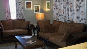 A living room with two brown leather sofas, a wooden coffee table, and a floor lamp. - Charming 2-bedroom cottage in welcoming Larned with AC,WiFi, full over full bunk (Larned)