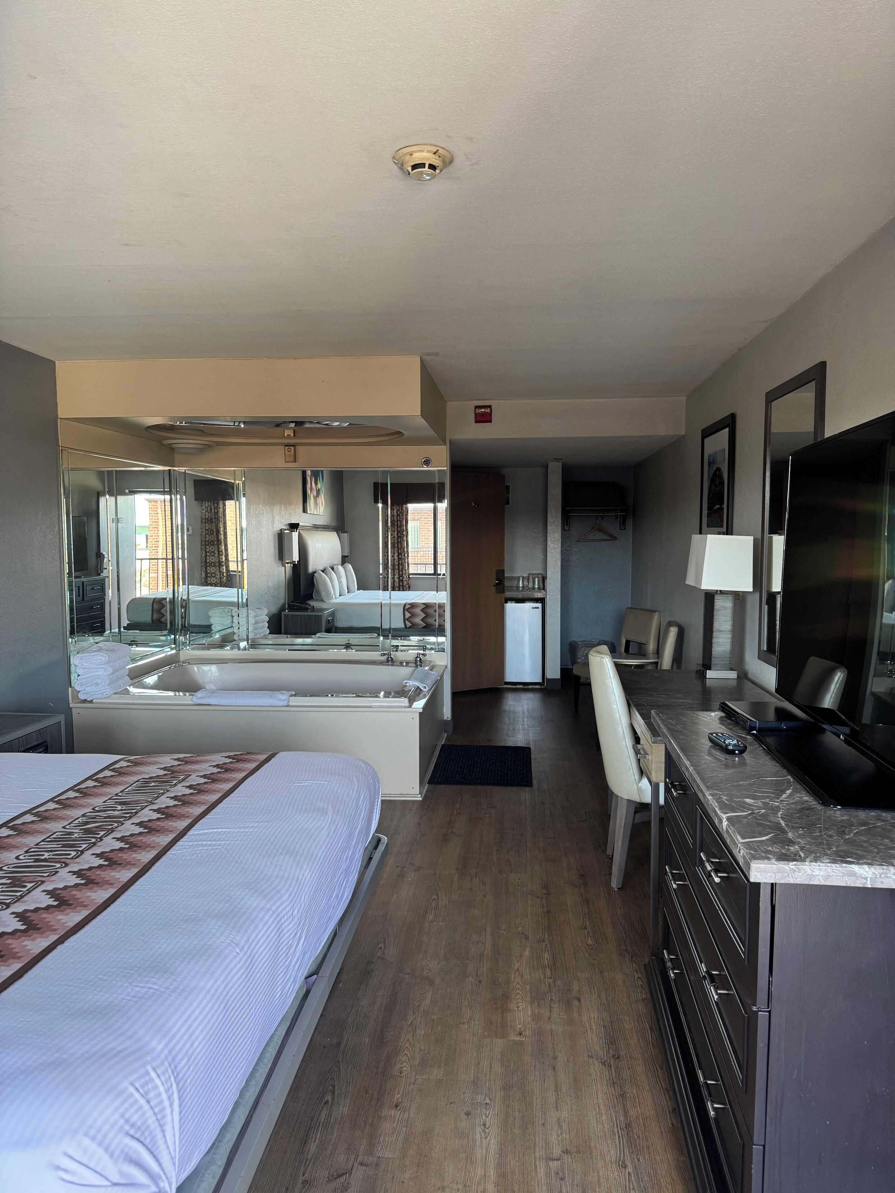 Ein Hotelzimmer mit Bett, Schreibtisch, Stuhl, Fernseher und einem Badezimmer mit Badewanne und Dusche.