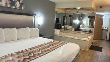 Quarto de hotel com uma cama grande, banheiro com paredes de vidro e um espelho refletindo o aposento.