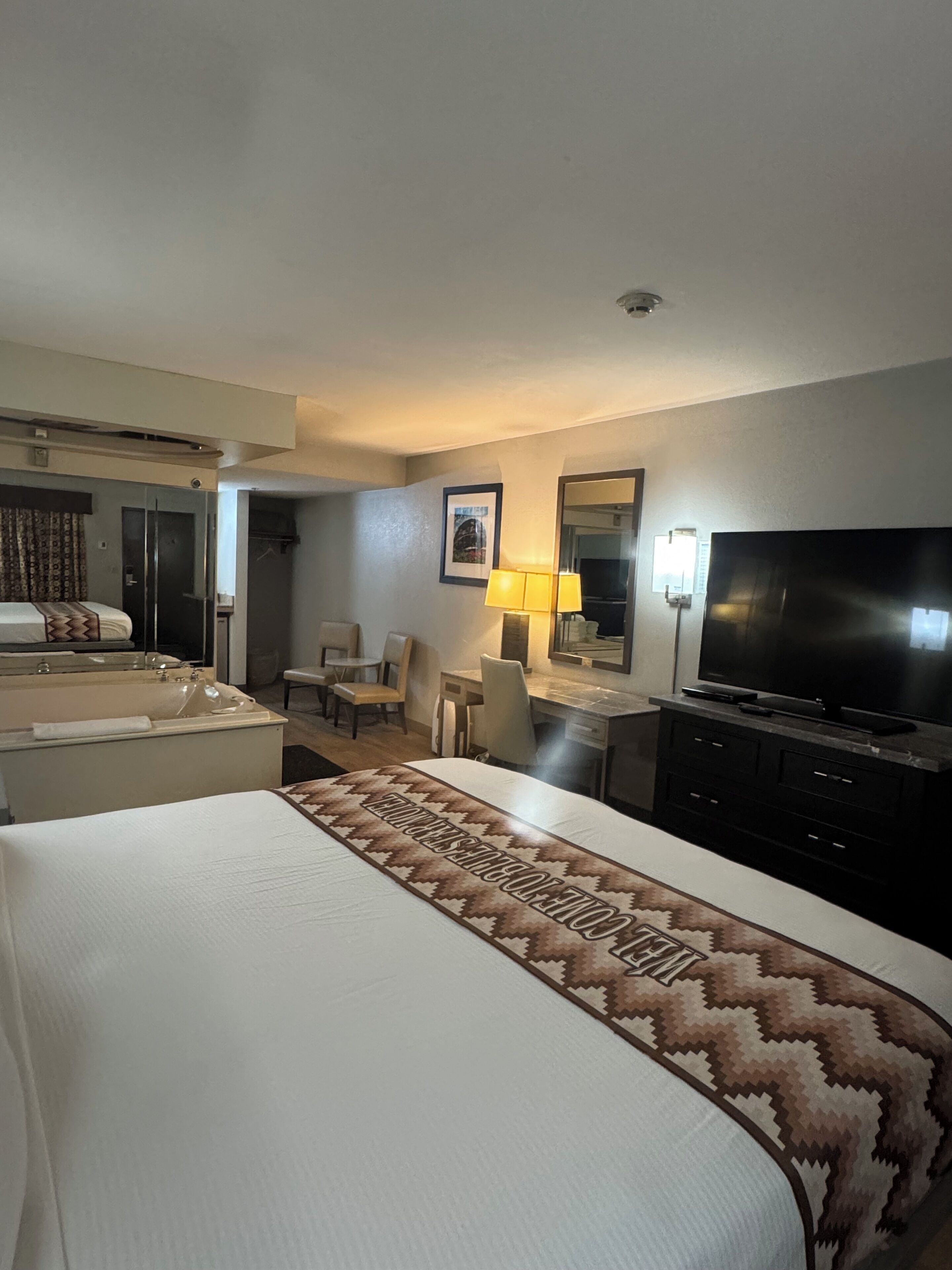 A hotel room with a large bed, a desk, a chair, a television, and a bathroom with a bathtub and shower.