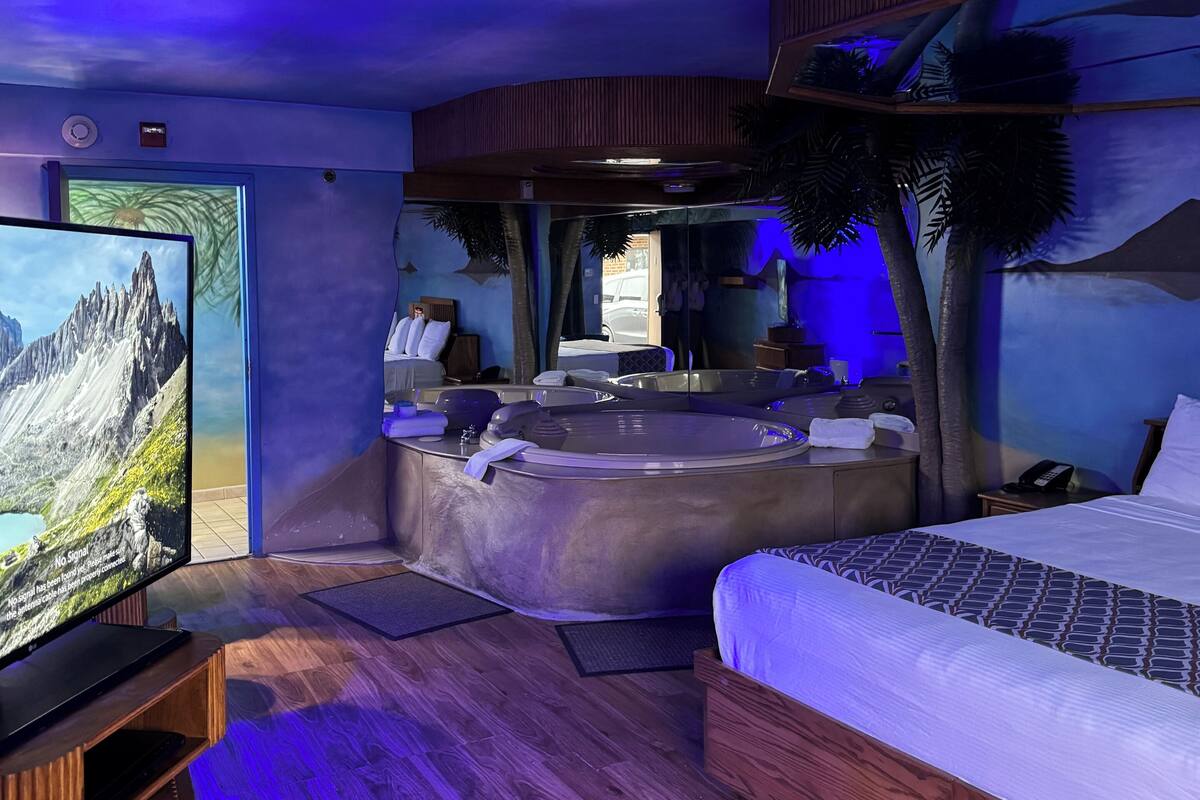 A modern hotel room with a large bed, a sitting area with a hot tub, a television, and a view of a mountain.