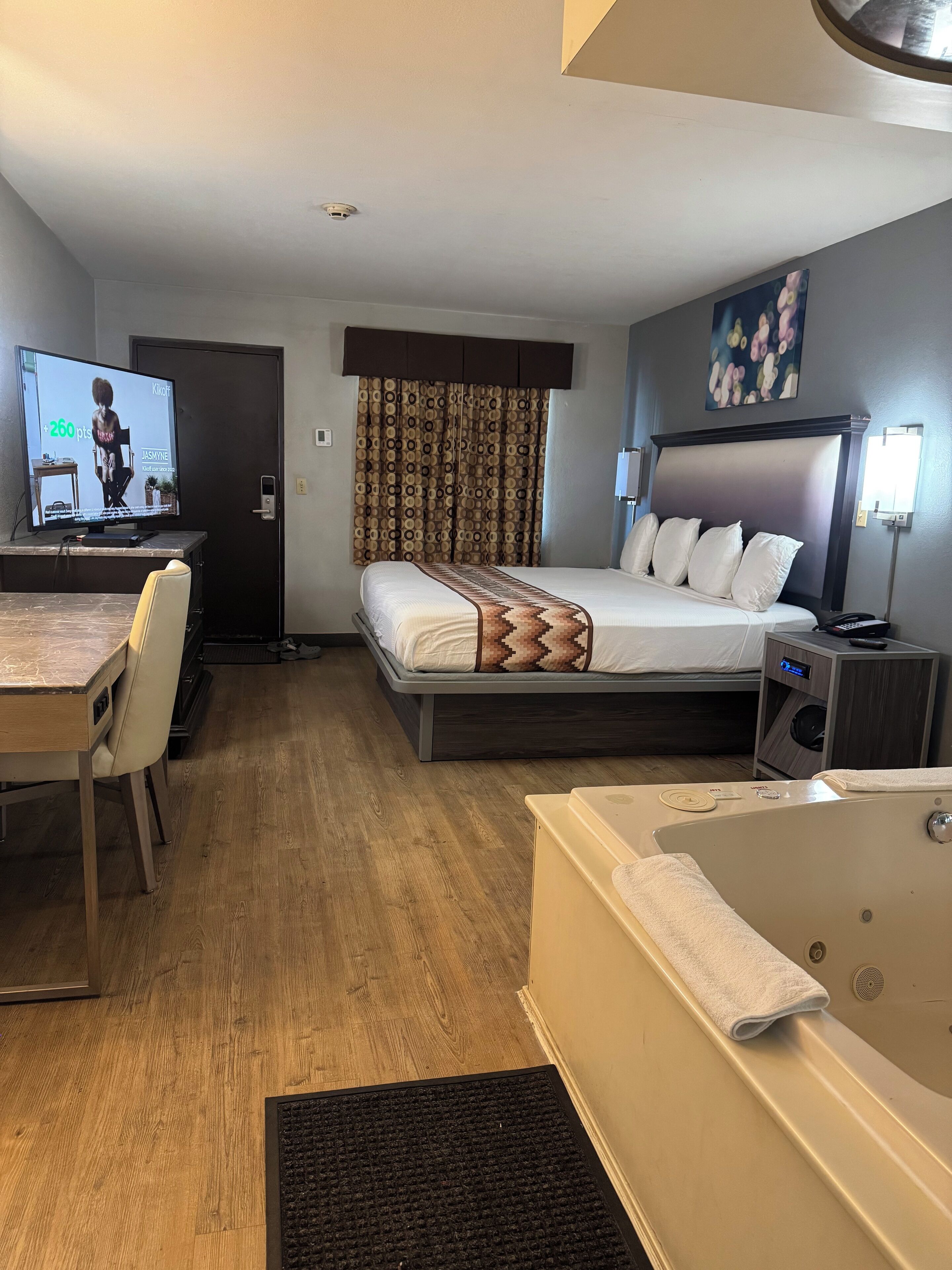 Een hotelkamer met een bed, een bureau, een televisie, een badkamer en een schilderij aan de muur.