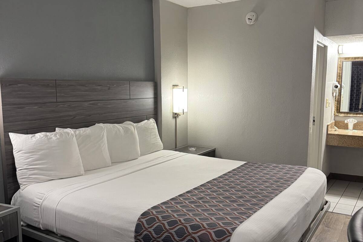 A hotel room with a large bed, a nightstand, a bedside lamp, and a mirror.