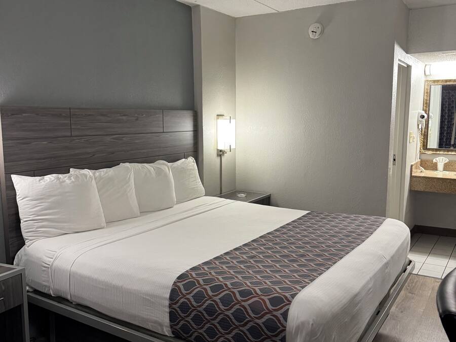 A hotel room with a large bed, a nightstand, a bedside lamp, and a mirror.