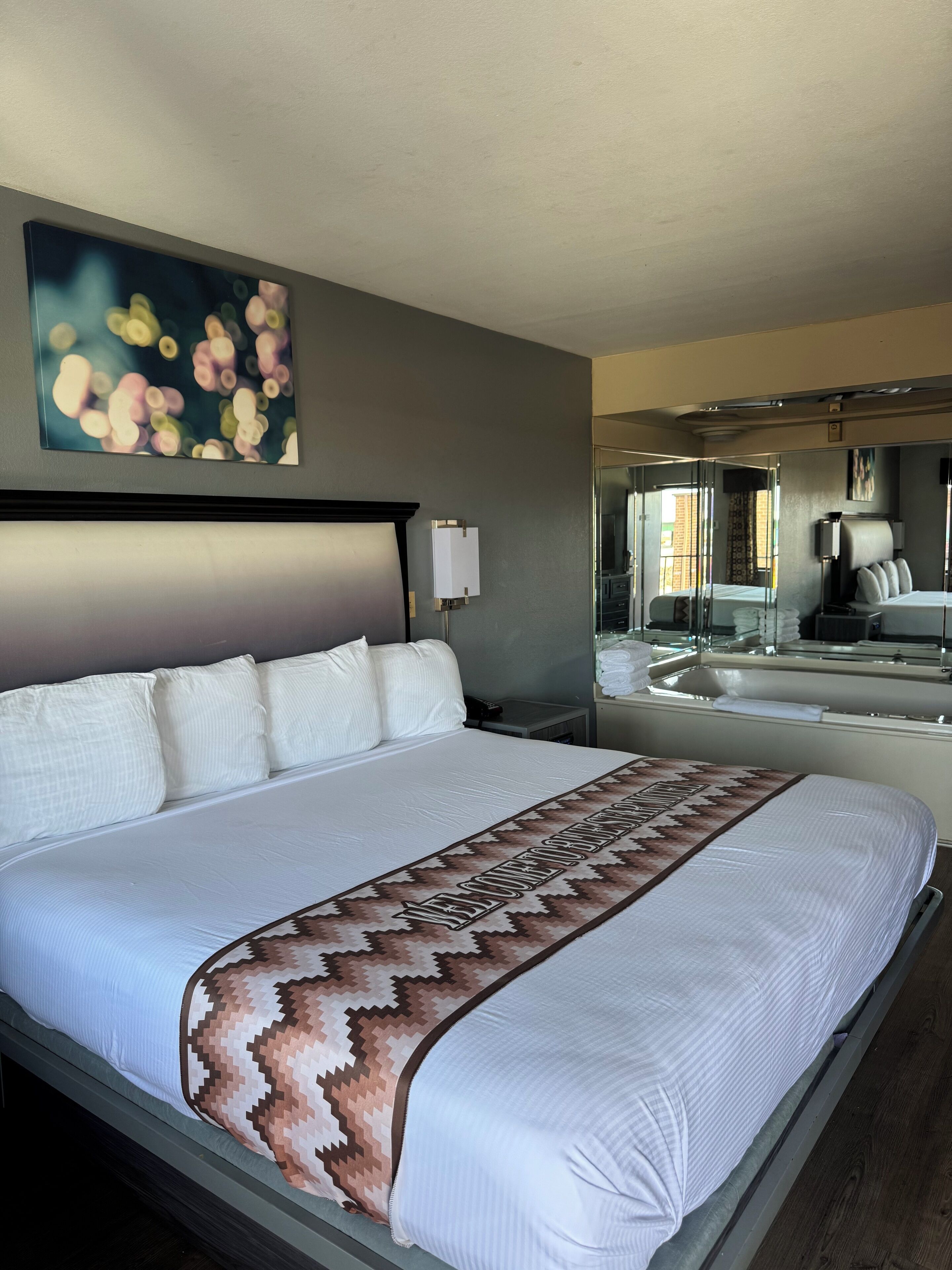 A hotel room with a large bed, a bedside table, a mirror, and a wall-mounted artwork.