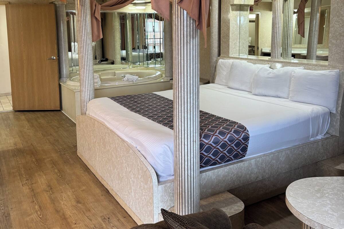 A four-poster bed with draped fabric, a marble-topped table, and a wooden floor.