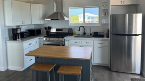 A modern kitchen with white cabinets, a stainless steel refrigerator, a built-in oven, and a wooden island with stools.
