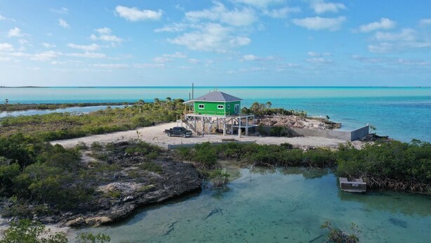 A green building with a dock, surrounded by clear blue water and vegetation.