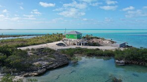 A green building with a dock, surrounded by clear blue water and vegetation. - Georgetown Exuma - Coconut Grove - Bonefish/skiff rental/blue hole/beach (George Town)