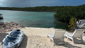 A kayak on a sandy beach with lounge chairs and a view of a calm sea and distant greenery.
