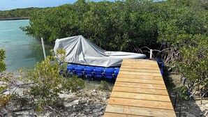 A wooden dock leading to a covered boat area with blue containers.