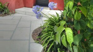 Een rood gebouw met een pannendak, een zwarte deur en kleine ramen. Er staan planten en bloemen voor het gebouw.