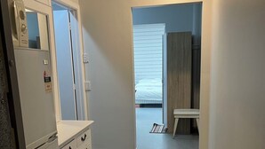 A compact kitchen with a refrigerator, a sink, and a countertop. There is a door leading to a bedroom with a bed and a window. - 3 single and 2 sofa beds Studio Suite 7 (Auckland)