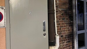 A grey utility meter box with the number 7, attached to a brick wall with a window and a door. - 3 single and 2 sofa beds Studio Suite 7 (Auckland)