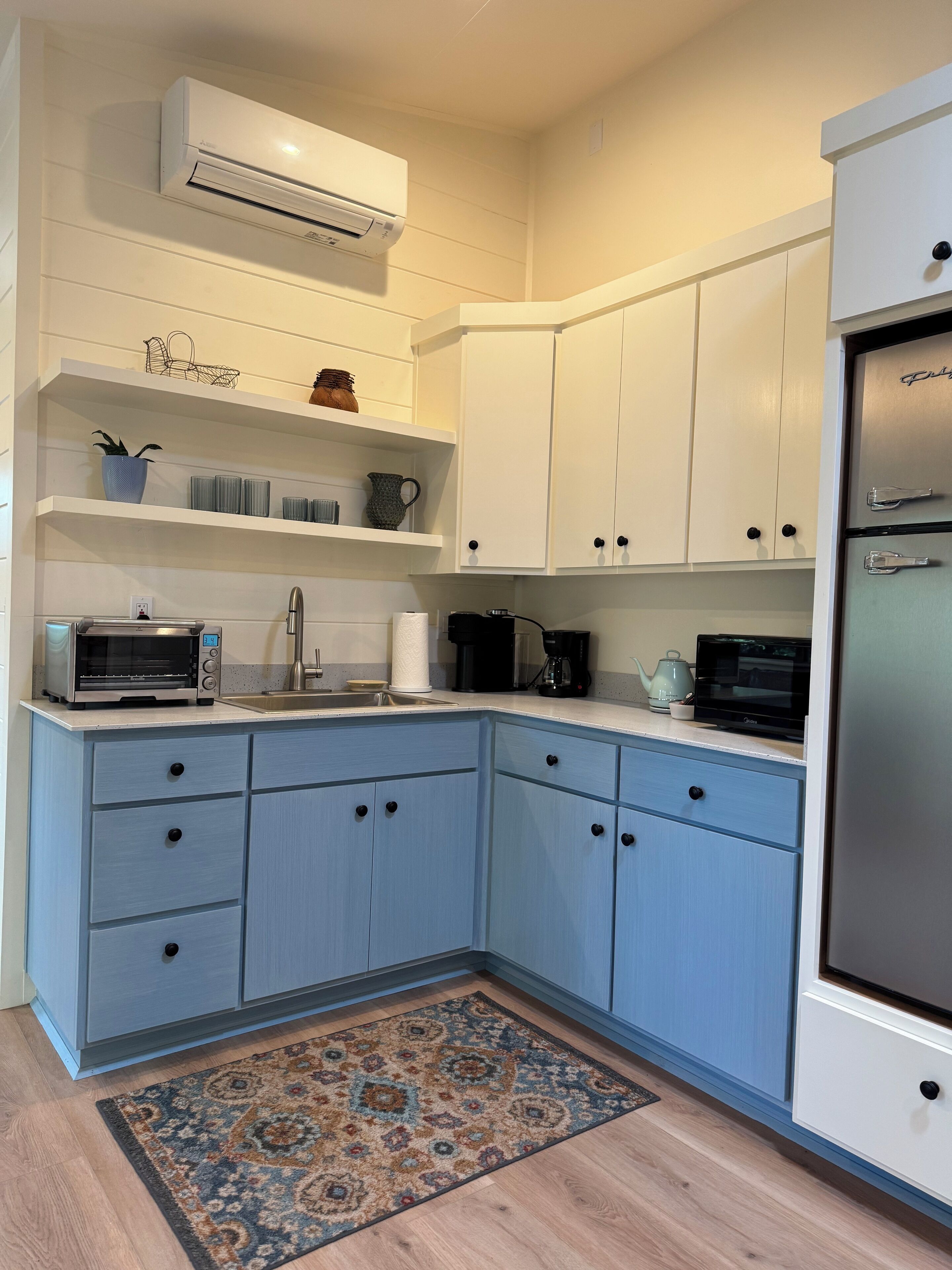 Una cocina moderna con armarios blancos, horno empotrado, microondas y refrigerador.