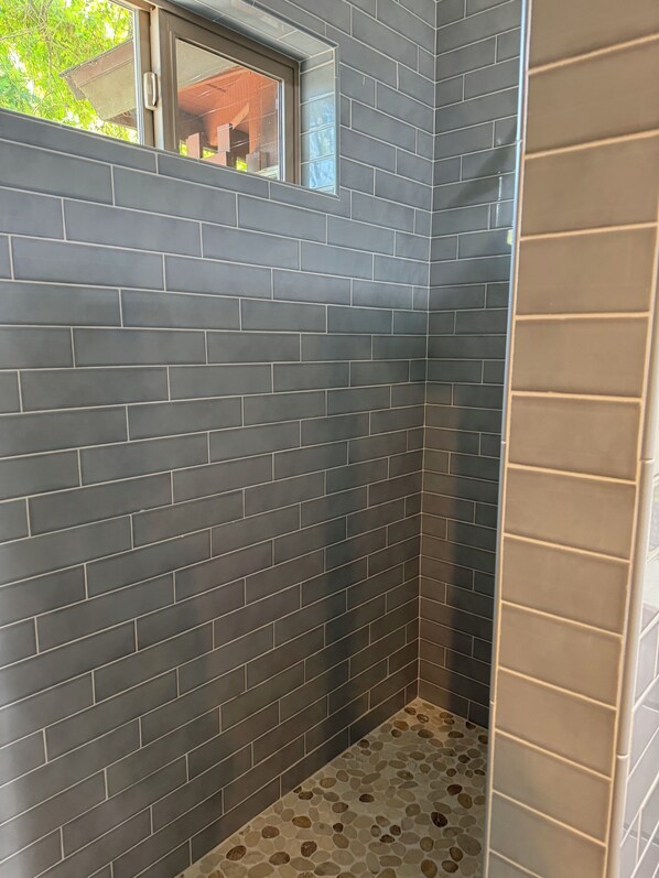 Un baño con paredes de azulejos gris oscuro y suelo con diseño de piedras.