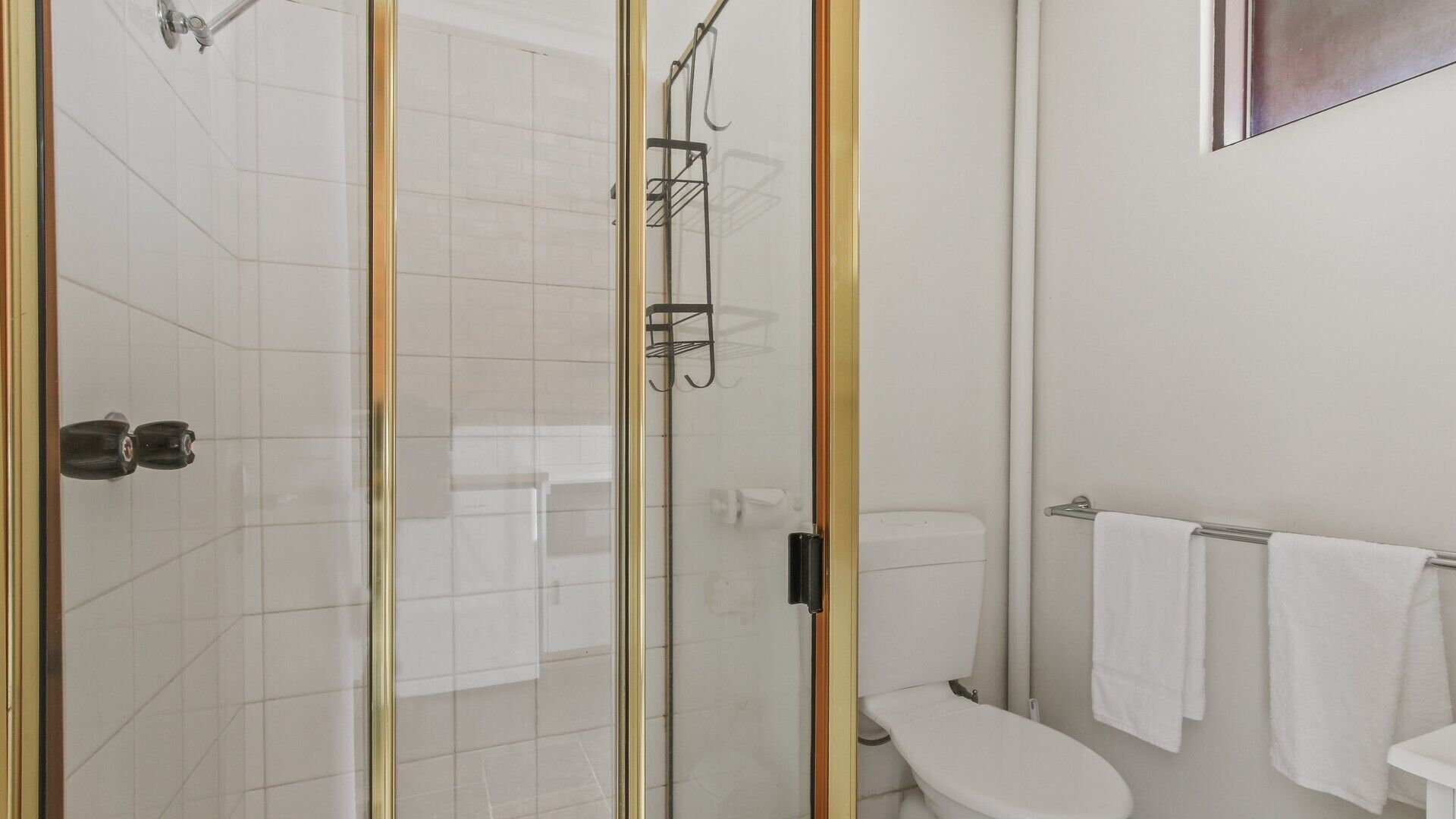 Un baño con ducha de vidrio, inodoro y lavabo con barra para toallas.