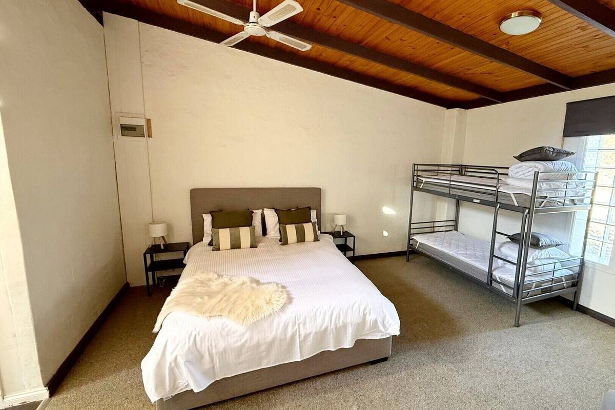 A bedroom with a single bed, a bunk bed, a ceiling fan, and a window with blinds.