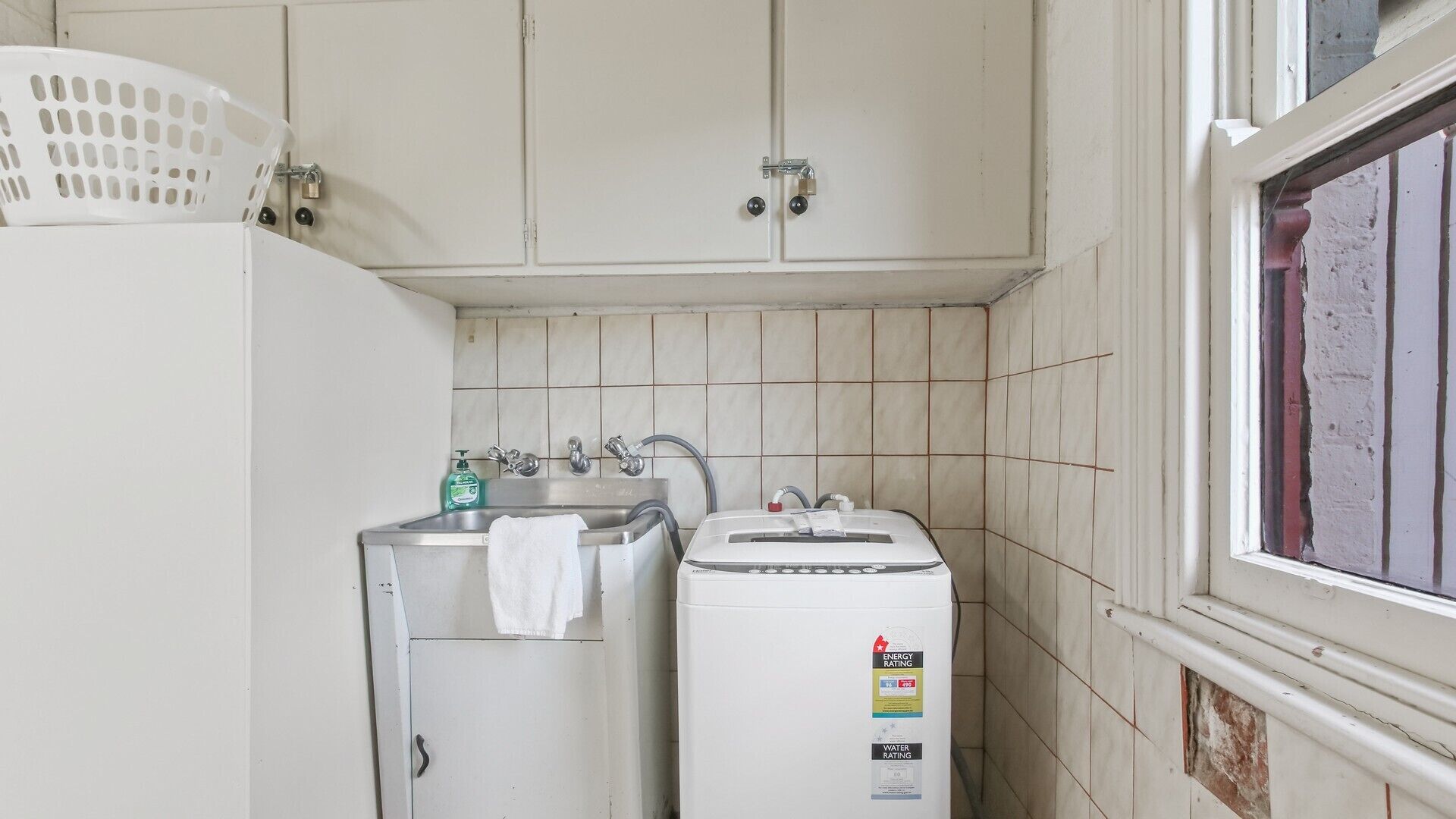 A small, compact kitchen with a washing machine, a sink, and a window.
