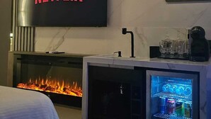 A modern hotel room with a flat-screen TV displaying the Netflix logo, a built-in fireplace, and a minibar. - Pousada Exclusive (Florianopolis)