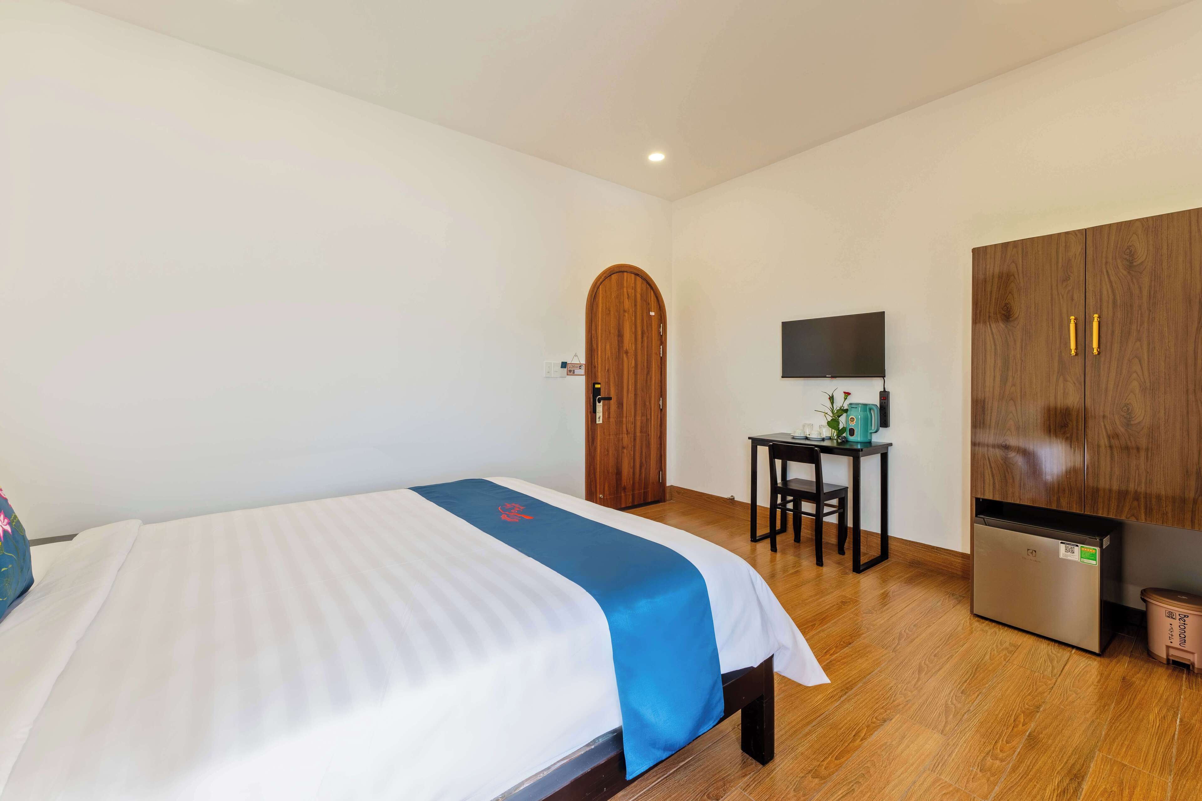 Quarto de hotel com cama, escrivaninha, televisão, guarda-roupa e frigorífico.