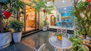 An indoor courtyard with potted plants, a round table with chairs, and a mural on the wall. - The View Boutique Hoi An (Da Nang)