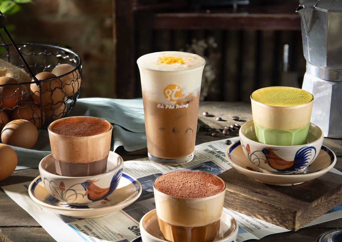Une table avec différentes sortes de boissons au café, un moulin à café et un panier d’œufs.