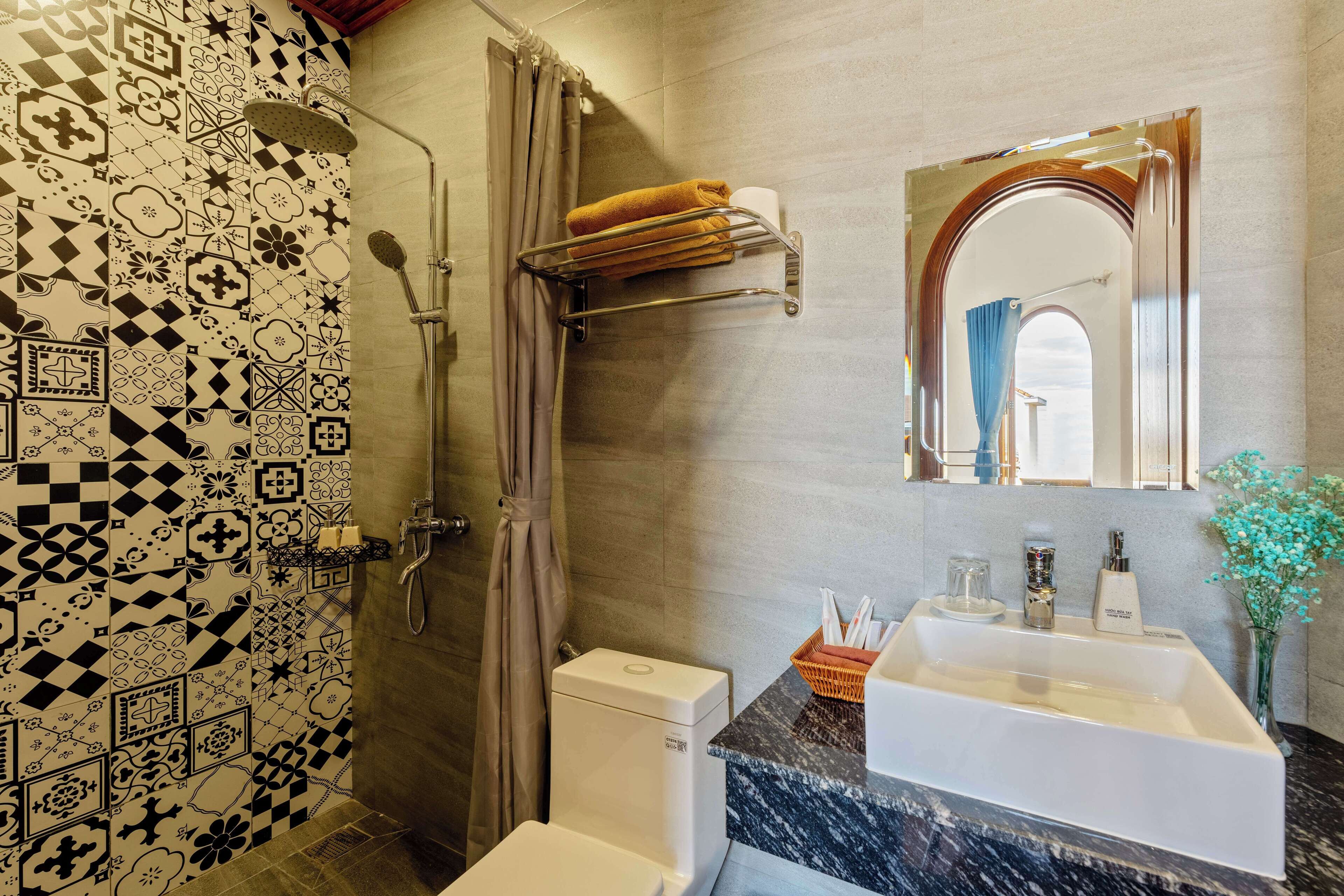 A bathroom with patterned tiles, a shower, a toilet, a sink with a marble countertop, and a mirror.
