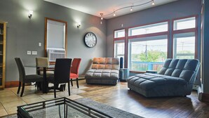 A living room with a large window, a clock, and a dining area with chairs. - 3 Min to Lake Michigan, 15 Min to Ski Crystal (X) (Elberta)