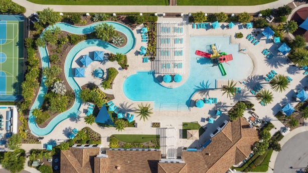 Vista aérea de un resort con una gran piscina, varias zonas de descanso y una cancha deportiva.