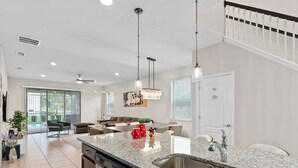 Una cocina amplia con encimeras de granito, pileta de acero inoxidable e iluminación colgante moderna.
