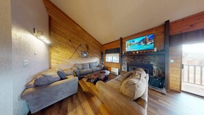 A cozy living room with a stone fireplace, wooden walls, and a large TV mounted above it. - Close to Lifts | Townhome | Angel View 2-3 (Angel Fire)