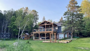 A two-story wooden house with a balcony, surrounded by a well-maintained lawn and trees. - Charming Country Oasis (Alton)