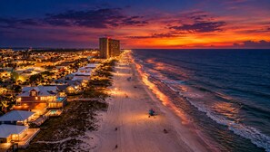Un pueblo costero al atardecer con playa, propiedades frente al mar y un hotel.