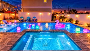Un área de piscina con sillones de descanso, un jacuzzi y luces decorativas.