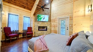 Ein Schlafzimmer in einer Blockhütte mit Kamin aus Stein, Deckenventilator und einem an der Wand befestigten Fernseher.