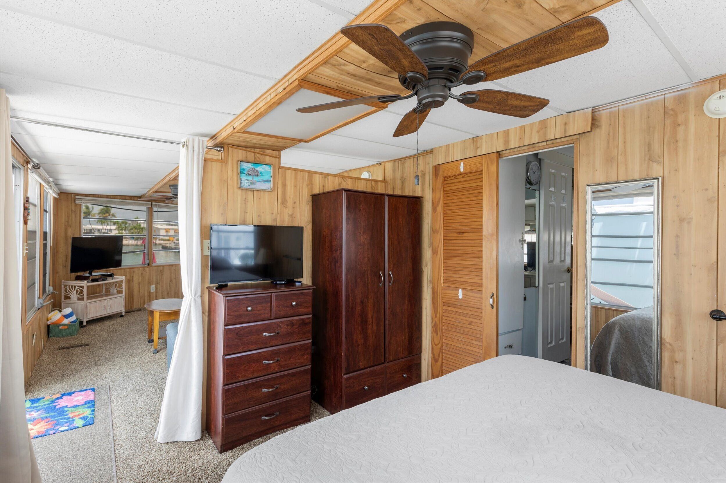 A bedroom with a ceiling fan, wooden wardrobe, a bed, and a television.