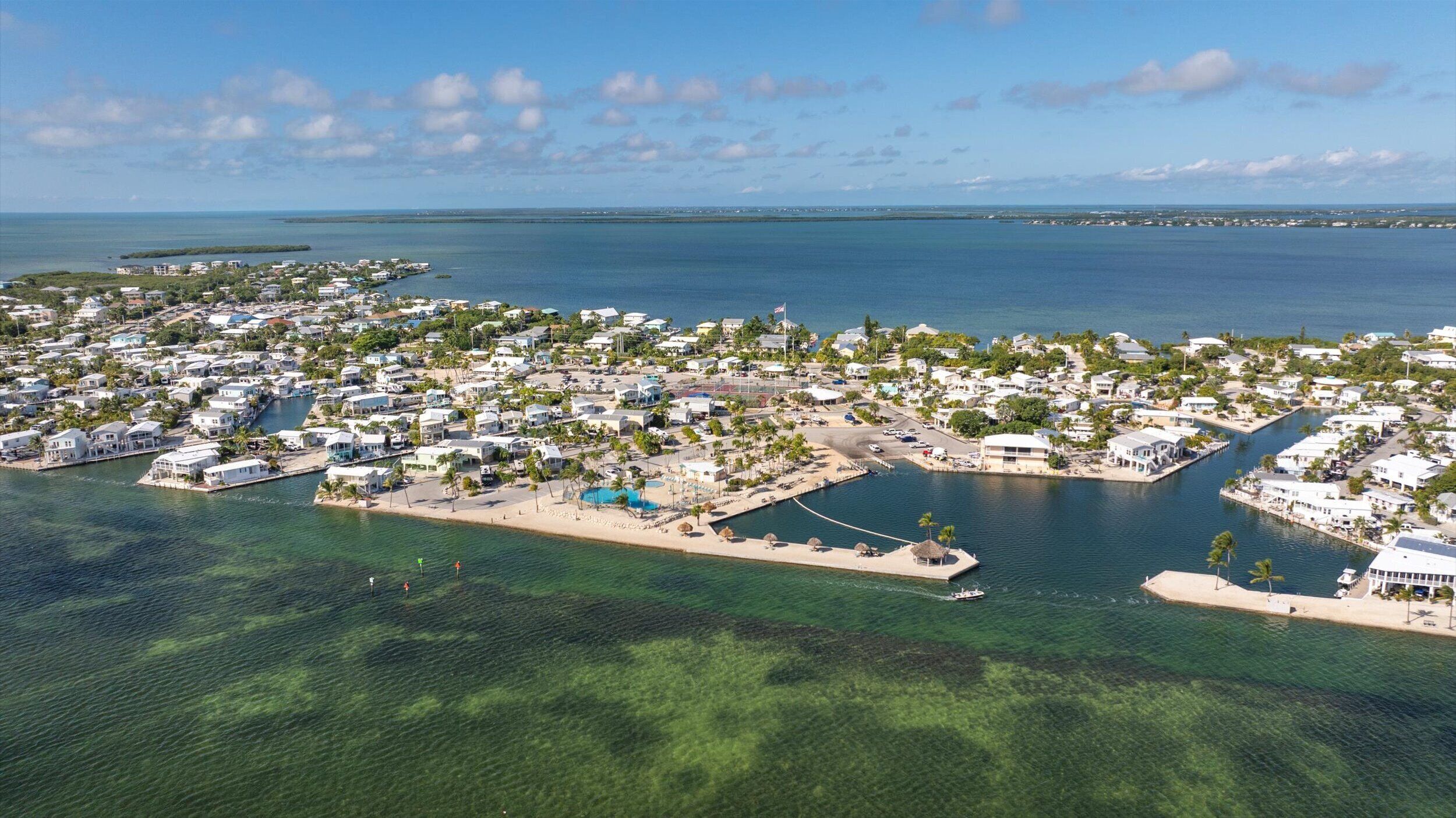 Vue aérienne d’une zone résidentielle côtière, avec des maisons, une eau d’un bleu limpide et un port de plaisance.