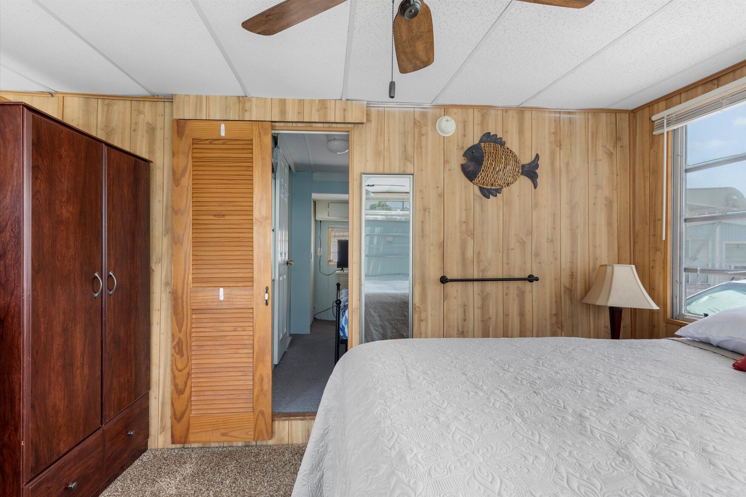 Ein Schlafzimmer mit einem Holzschrank, einem Bett mit einer strukturierten Decke, einer Wanddekoration mit Fischmotiv und einem Fenster mit Aussicht.