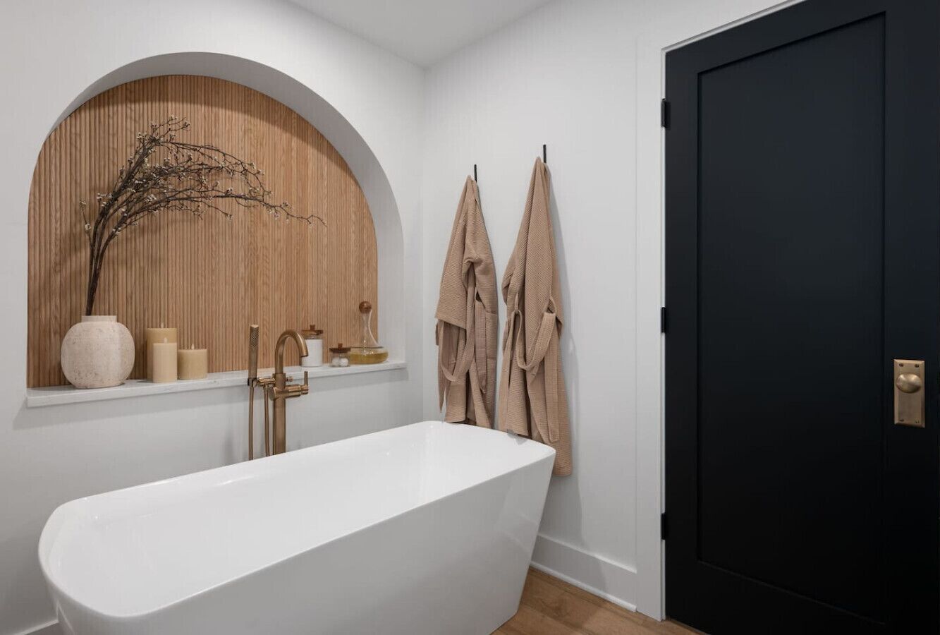Une salle de bain moderne avec une baignoire sur pieds, un meuble-lavabo en bois et une porte noire.