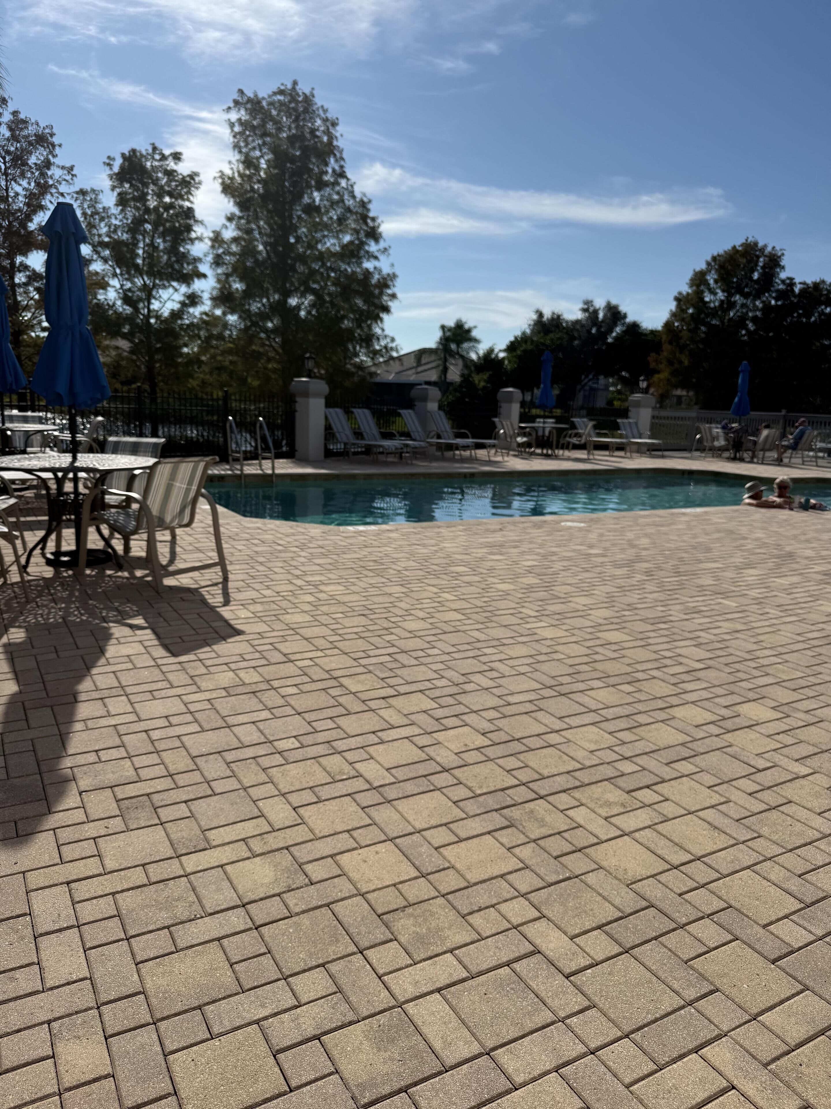 A pool area with tiled flooring, lounge chairs, and umbrellas.