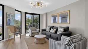 A modern living room with a grey sofa, striped armchairs, a round coffee table, and a ceiling light fixture. - Beachfront, Pool Access, Balcony w/ Oceanview 222 D Shipwatch by Avantstay (Isle of Palms)