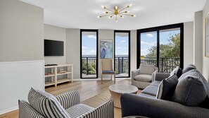 A modern living room with a sofa, armchairs, a coffee table, a TV, and a balcony with a view. - Beachfront, Pool Access, Balcony w/ Oceanview 222 D Shipwatch by Avantstay (Isle of Palms)