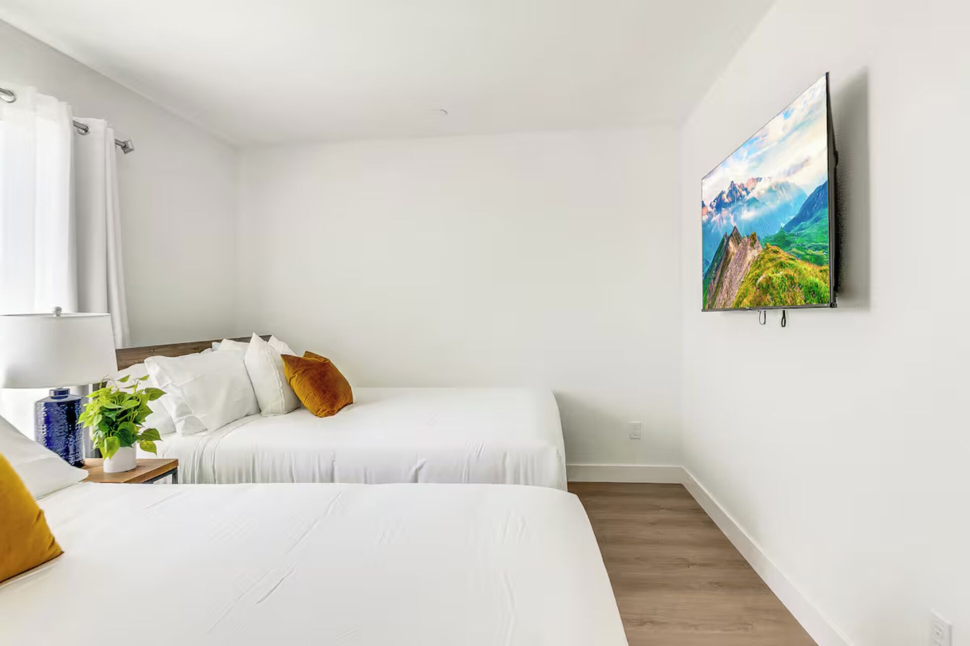 Une chambre à coucher au style minimaliste, avec deux lits, un tableau accroché au mur et une table de chevet sur laquelle se trouvent une lampe et une plante.