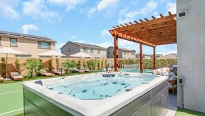 Ein Whirlpool mit einer Holzhütte darüber, umgeben von Liegestühlen und Sonnenschirmen, mit einem Pool im Hintergrund.